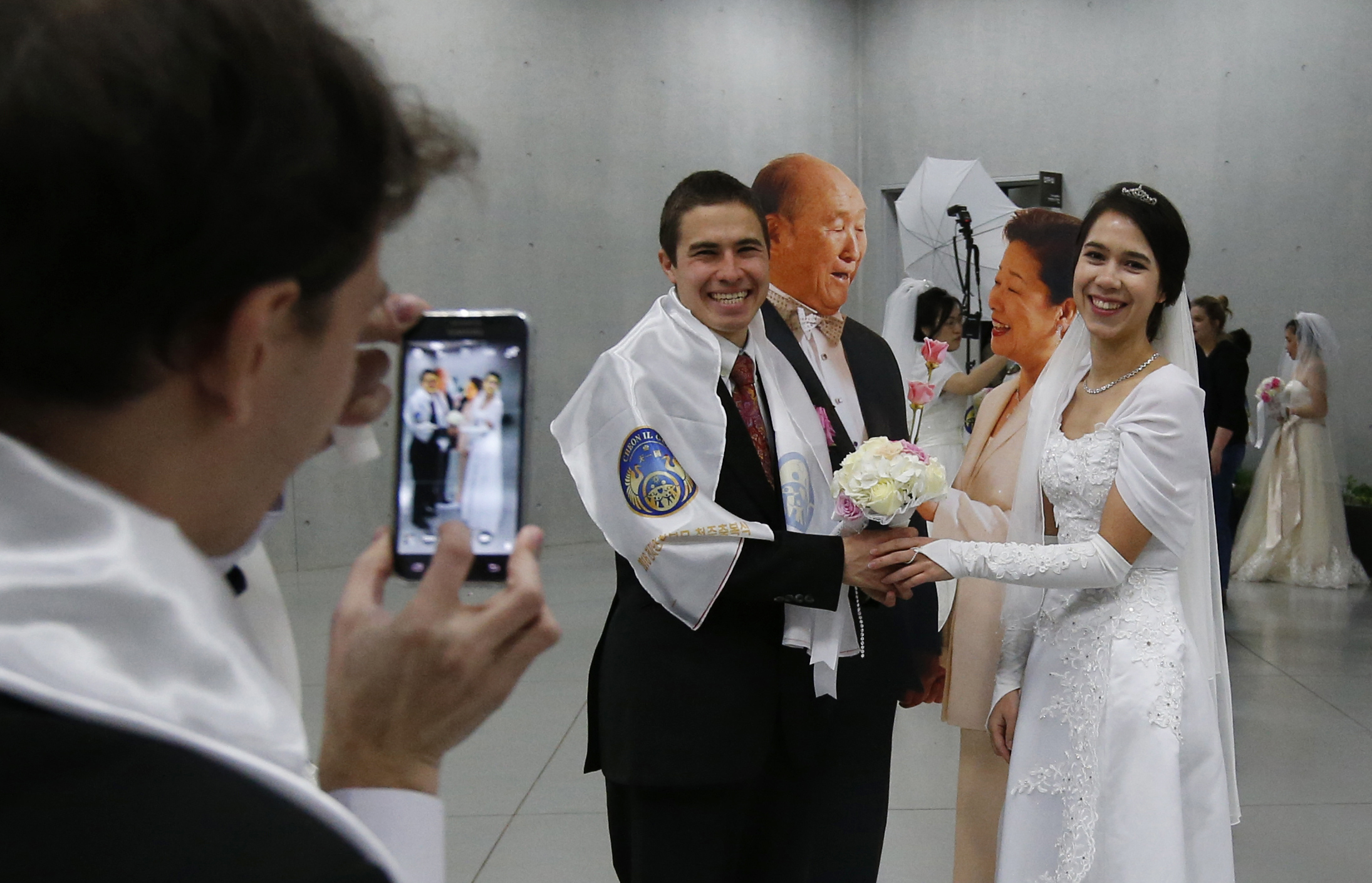 A couple have their souvenir photo taken near the cutout pictures of late Rev. Sun Myung Moon, the founder of the Unification Church and wife Hak Ja Han Moon before their mass wedding ceremony at the Cheong Shim Peace World Center in Gapyeong, South Korea, Saturday, Feb. 20, 2016. Three thousand of couples from more than 60 countries attended and other 12,000 couples participated in the Unification Church's mass wedding via live-streamed broadcast, according to the church, arranged by Hak Ja Han Moon. (AP Photo/Lee Jin-man) South Korea Mass Wedding