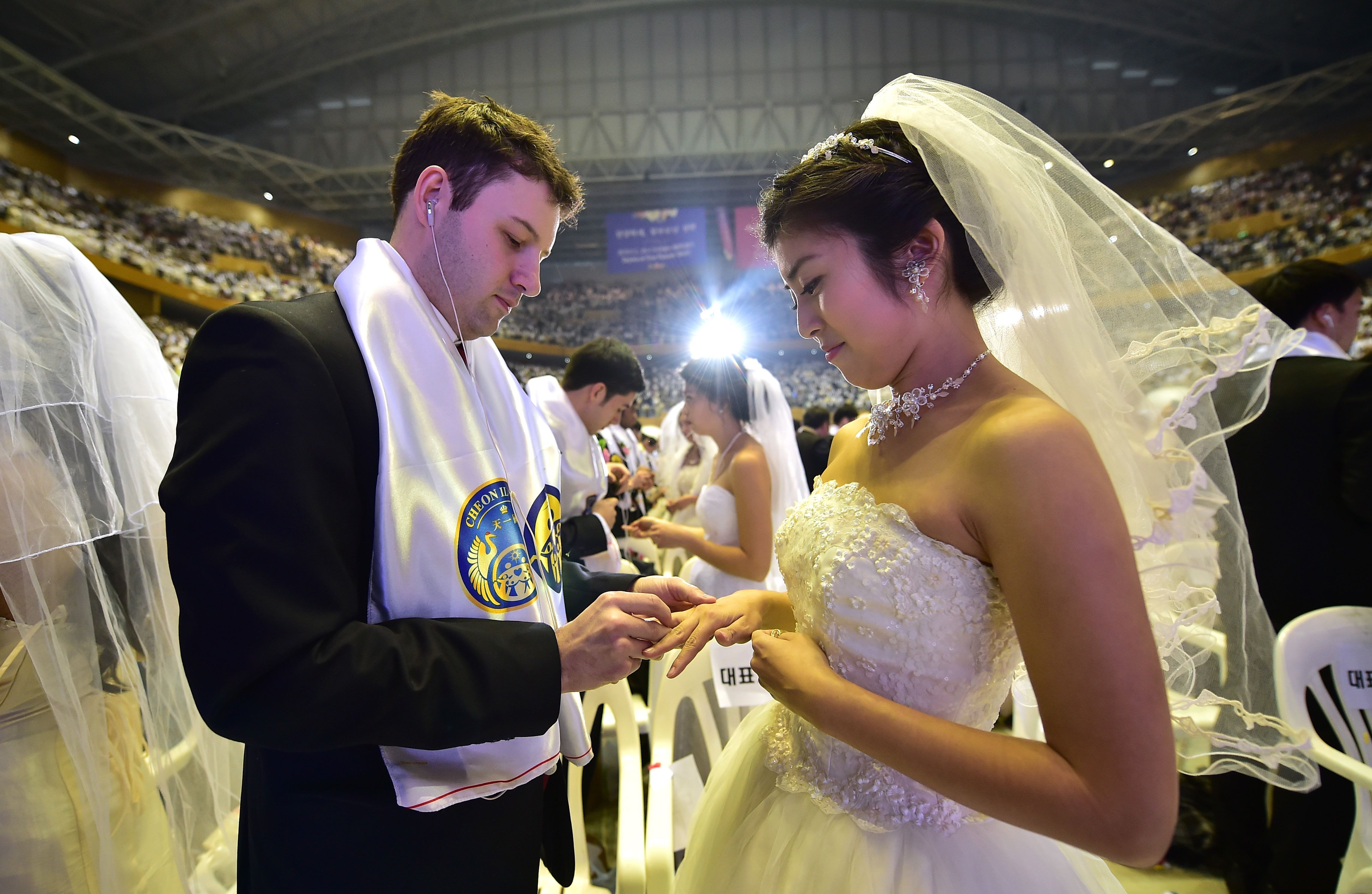 A groom puts a ring on the finger of his bride during a mass wedding held by the Unification Church at Cheongshim Peace World Center in Gapyeong, east of Seoul, on February 20, 2016. Hundreds of couples were married at the South Korean headquarters of the Unification Church. The Unification Church, set up by Sun Myung Moon in Seoul in 1954, is one of the world's most controversial religious organisations, and its devotees are often dubbed "Moonies" after the founder. AFP PHOTO / JUNG YEON-JE SKOREA--RELIGION-UNIFICATION-MARRIAGE