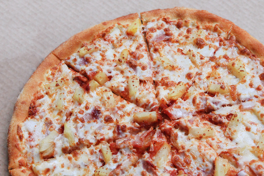 Pineapple Pizza or Hawaiian Pizza with Cheese, Pineapple, Tomato Original Sauce, Bacon or Ham Toppings. Close Up View of Freshly Cooked Tasty Pizza Pie on Thin Dough with Chunks in Delivery Box.